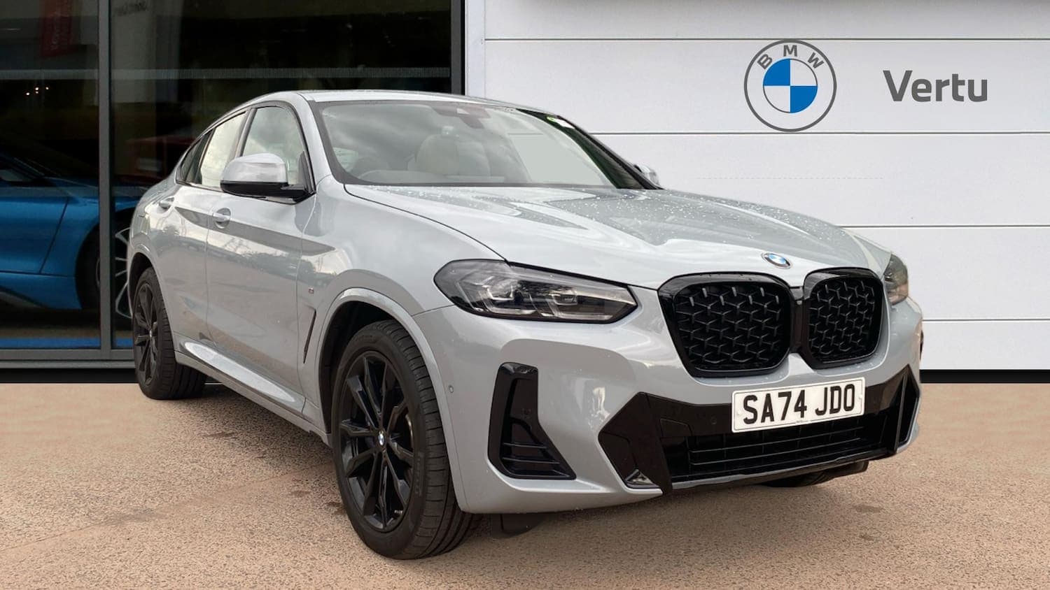 The grey X4 at front three-quarter outside a BMW dealership, black kidney grille and black 20-inch wheels